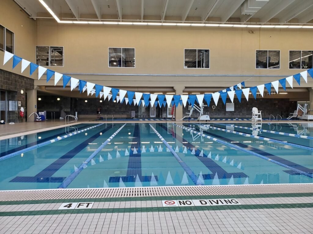 Indoor lap pool with lane lines, blue and white pennant flags and a no diving marking on the pool deck