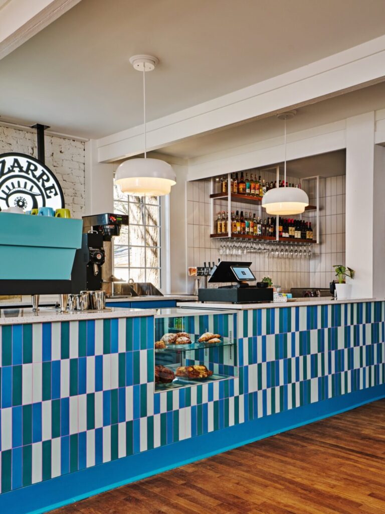 Colorful coffee bar inside Bizarre Coffee in downtown Roswell, Georgia, featuring a striped counter, espresso machine, pastry display, and shelves of bottles behind the bar.