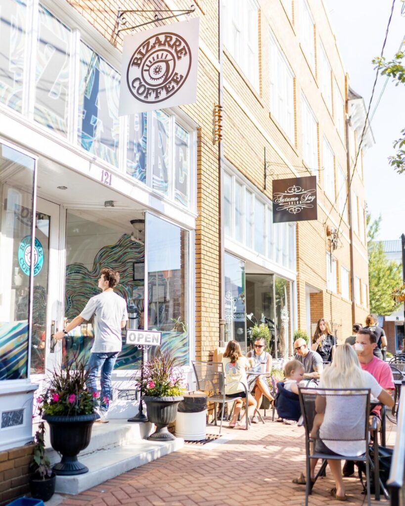 Customers sit at outdoor tables along the sidewalk outside Bizarre Coffee in downtown Roswell, Georgia, beneath the café’s hanging sign.