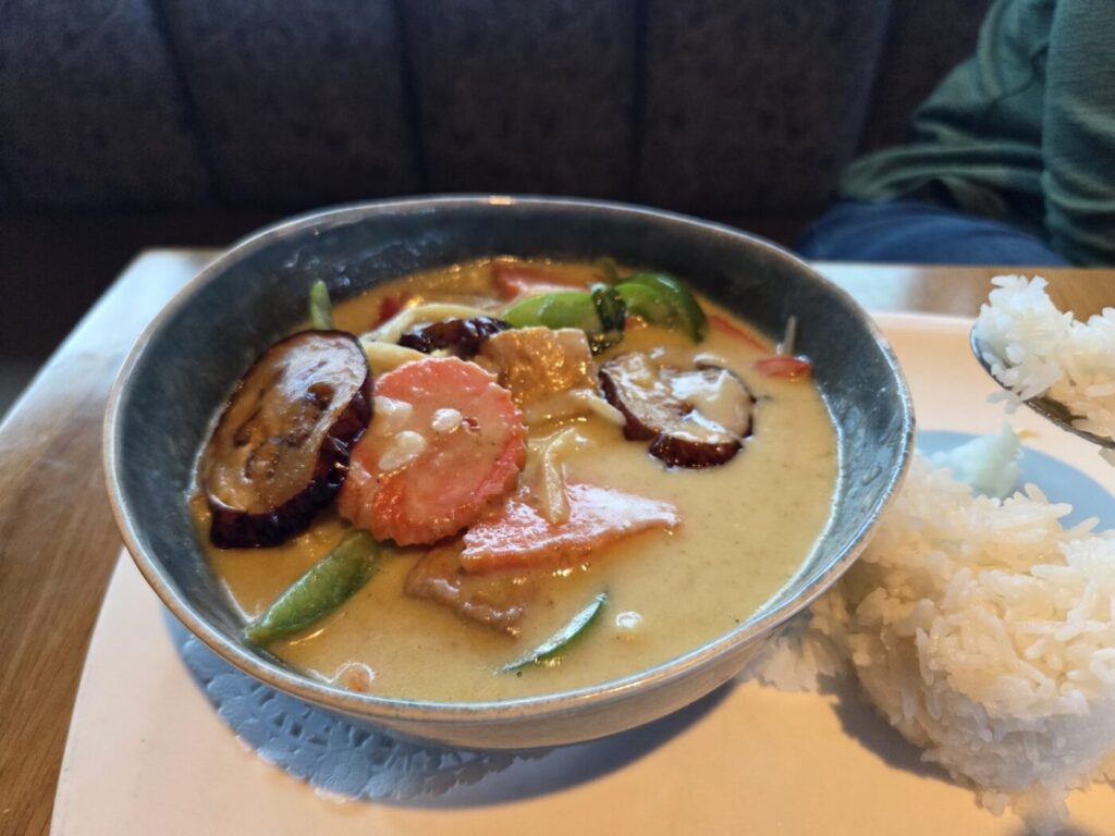 Bowl of Thai curry with vegetables and chicken, served with a side of white rice in a restaurant setting