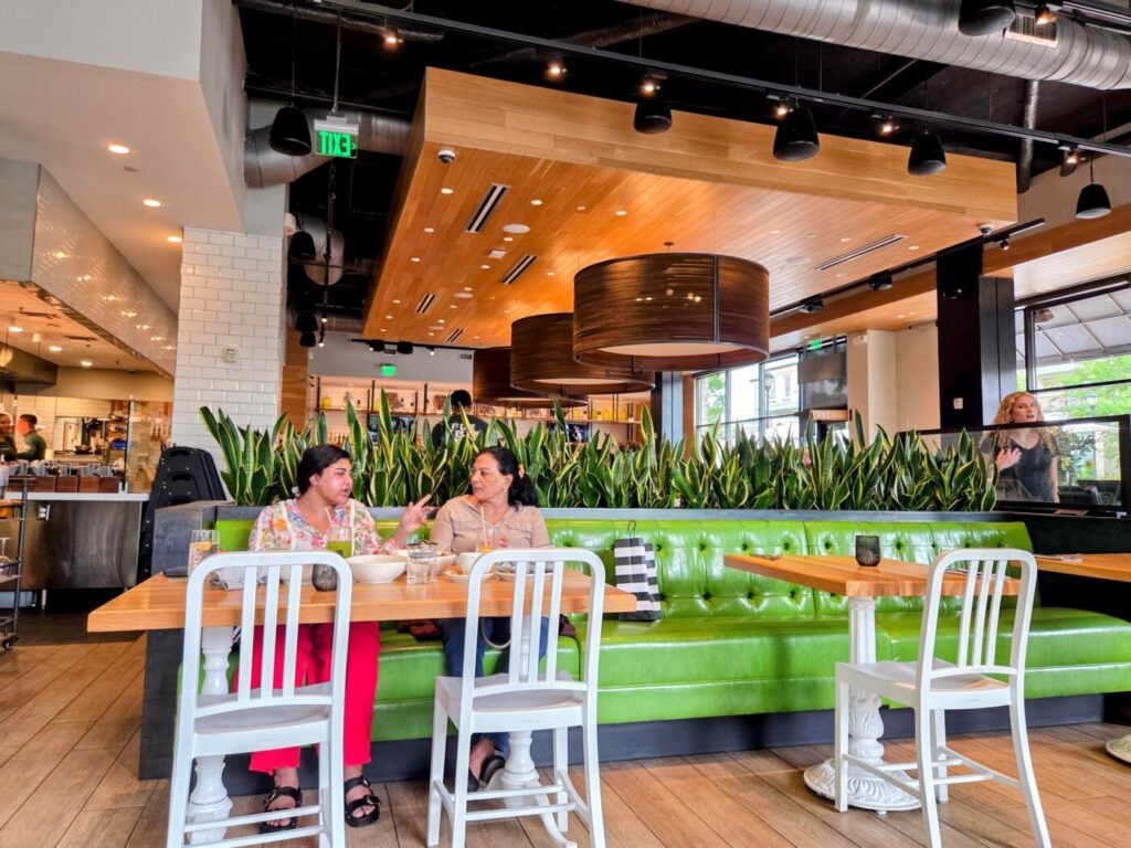 Interior of True Food Kitchen in Avalon with diners seated at a green booth, surrounded by plants and warm wood ceiling lighting