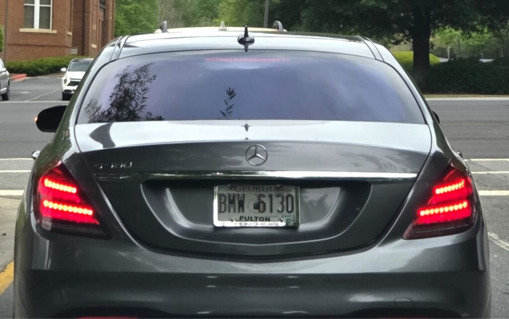 Close-up of a Mercedes-Benz with a standard Georgia license plate stopped near a Baptist church in Johns Creek, the plate number forming an ironically meaningful combination.