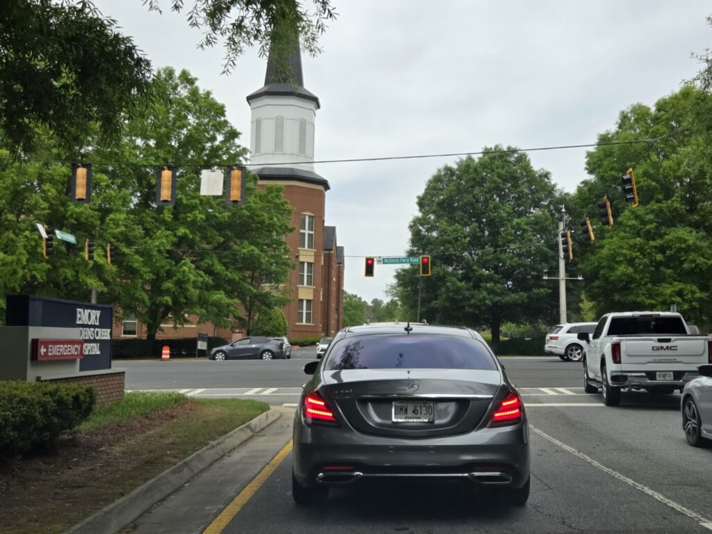 A car with a standard Georgia license plate waits on McGinnis Ferry Road in Johns Creek, near a Baptist church