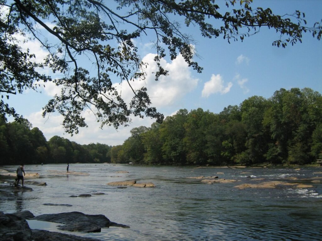Wide river with shallow water, rocks and a few people standing near the shore