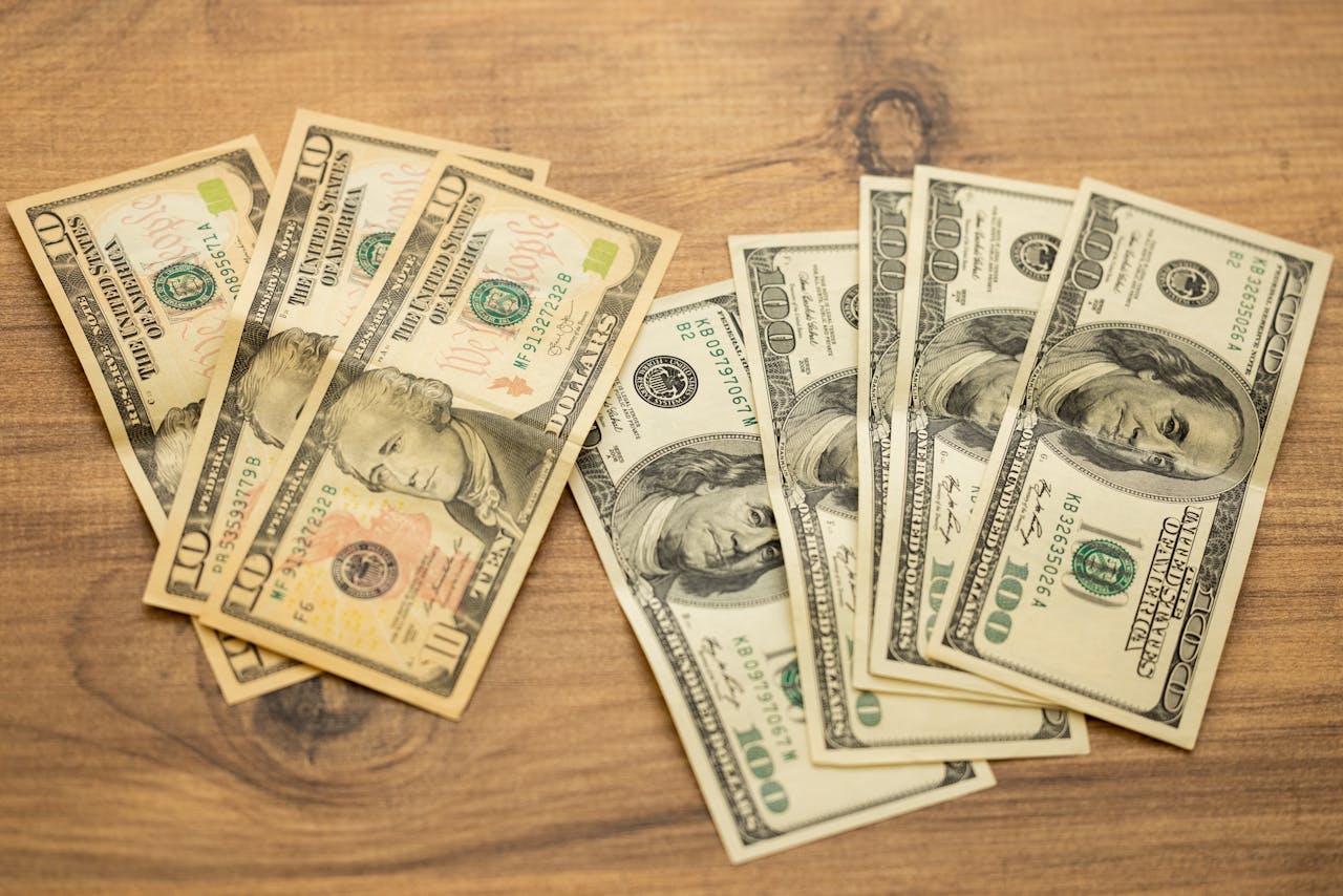 Stacks of U.S. ten- and hundred-dollar bills on a wooden surface.