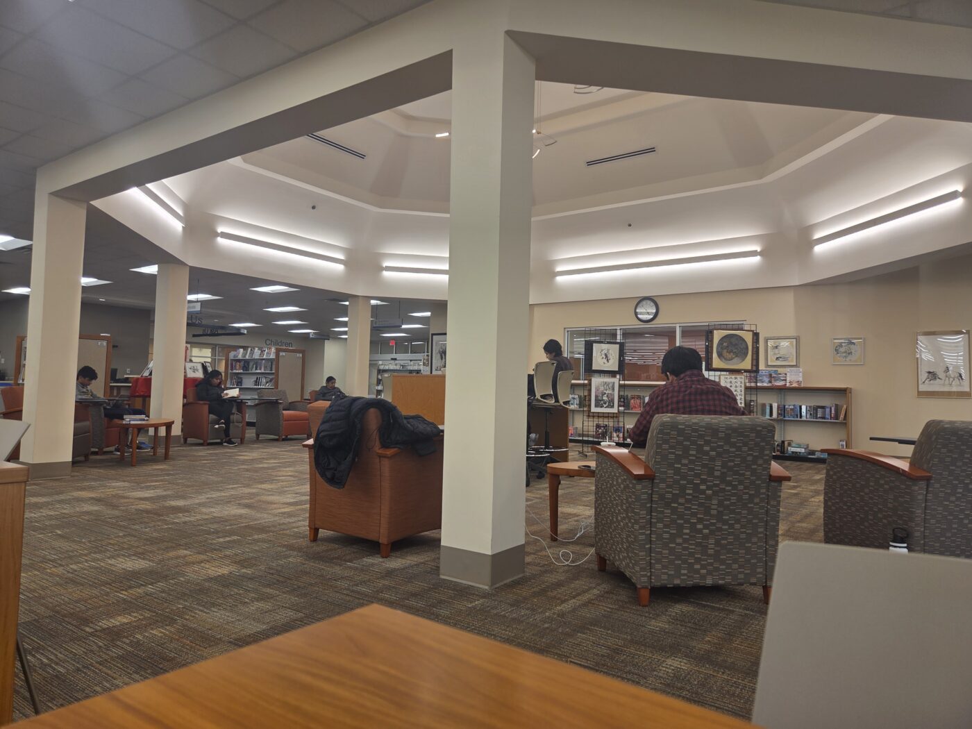 People seated in a library reading area with chairs, tables and bookshelves