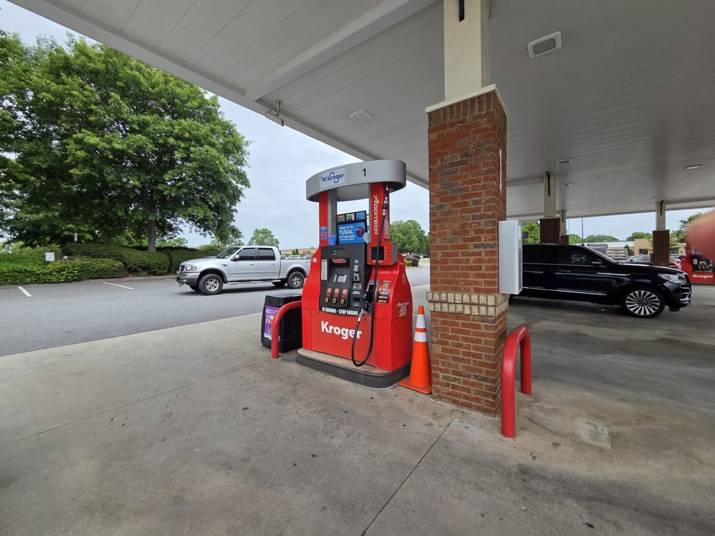 A Kroger gas pump under a canopy with vehicles nearby