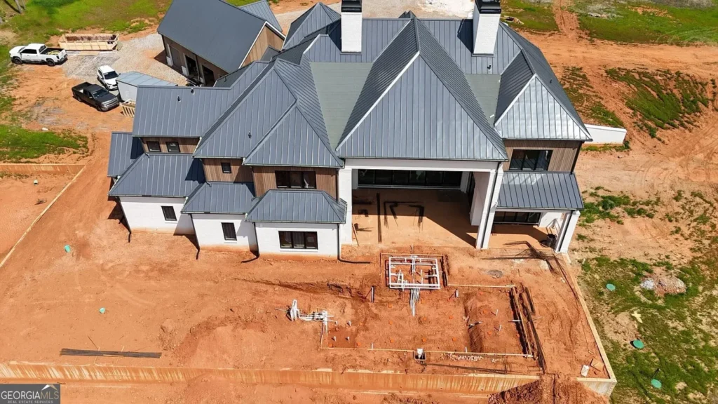 Aerial close-up of a large luxury home under construction in Milton, Georgia, with a metal roof, unfinished grounds and construction equipment around the property.
