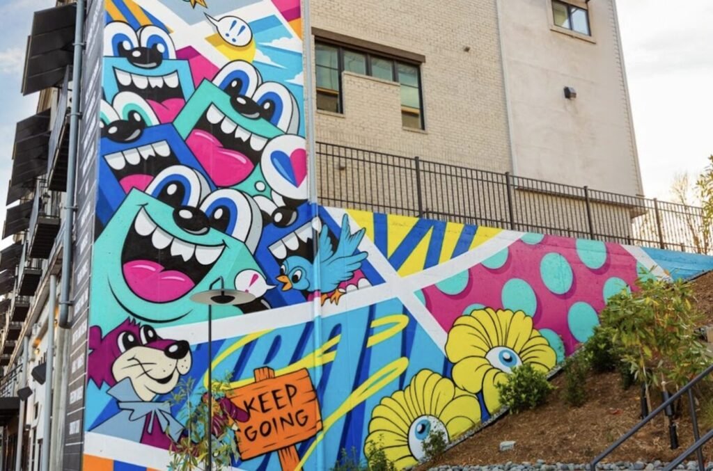Large colorful mural by Atlanta artist Greg Mike featuring cartoon-inspired characters and bold geometric patterns on the side of a building