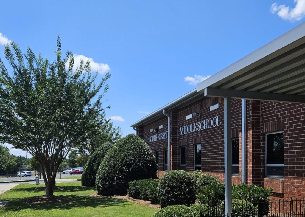 Brick middle school building with trees and shrubs outside under a blue sky