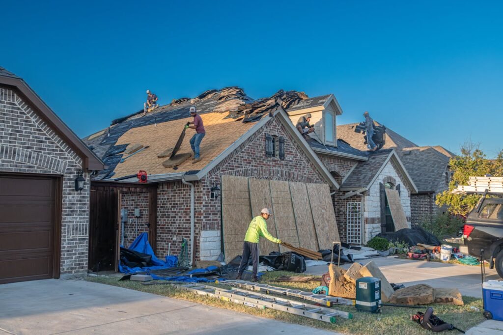 Roofing crew working on a large suburban house with sections of the roof stripped back and covered with plywood.