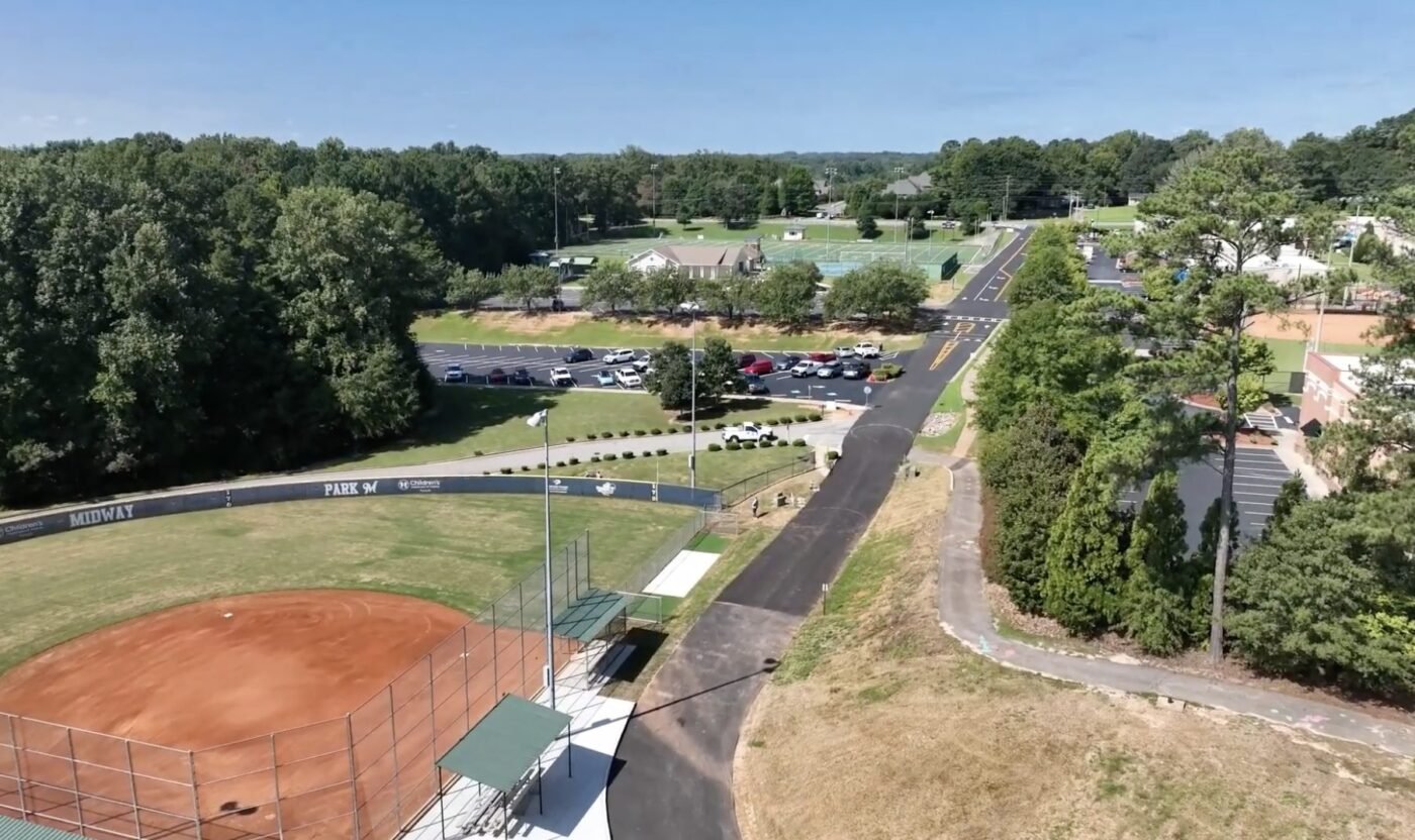 Aerial view of a baseball field, parking lot, and road lined with trees