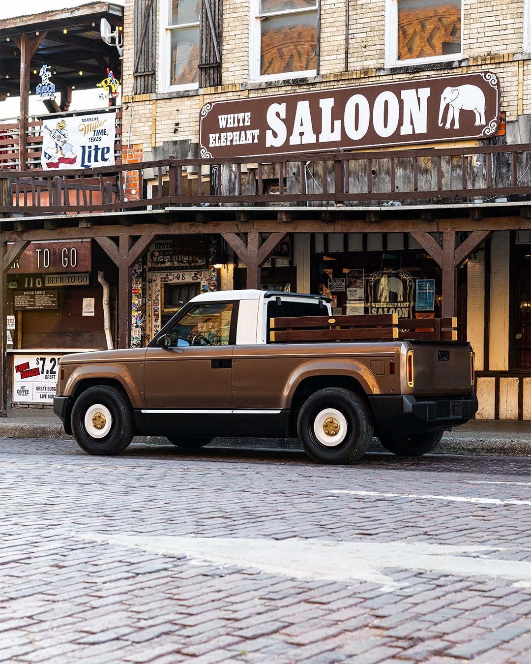 A small brown pickup truck parked in front of a bar with a large White Elephant Saloon sign.