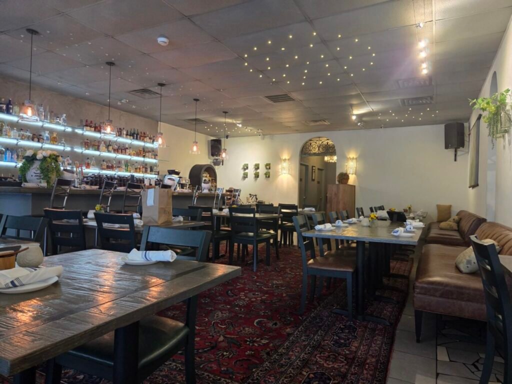 Noosh Kitchen dining room with set tables, Persian rugs, a bar and warm ceiling lights.