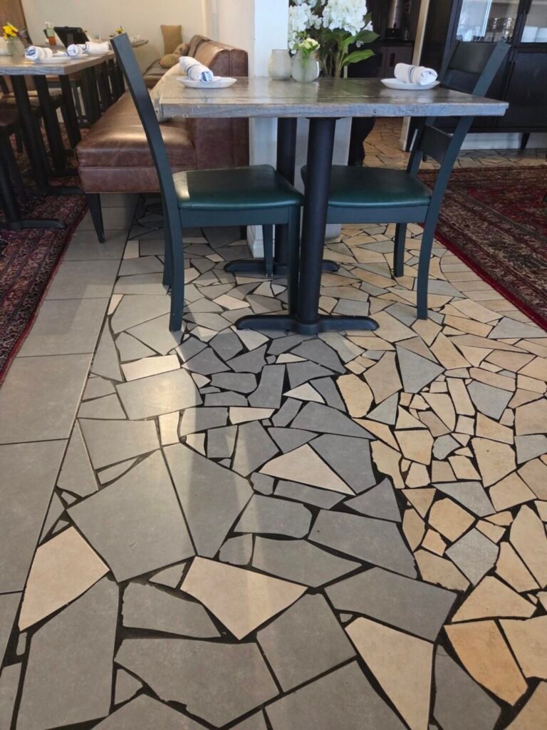 Restaurant table and chairs over a floor made from irregular broken tile pieces beside conventional square tiles.