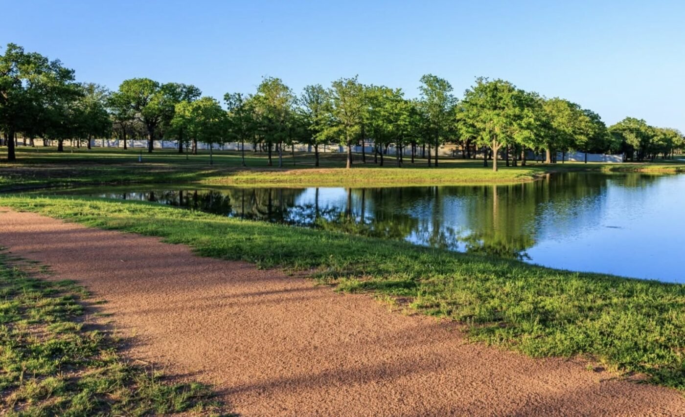 Curved walking path beside a pond with trees reflected in the water