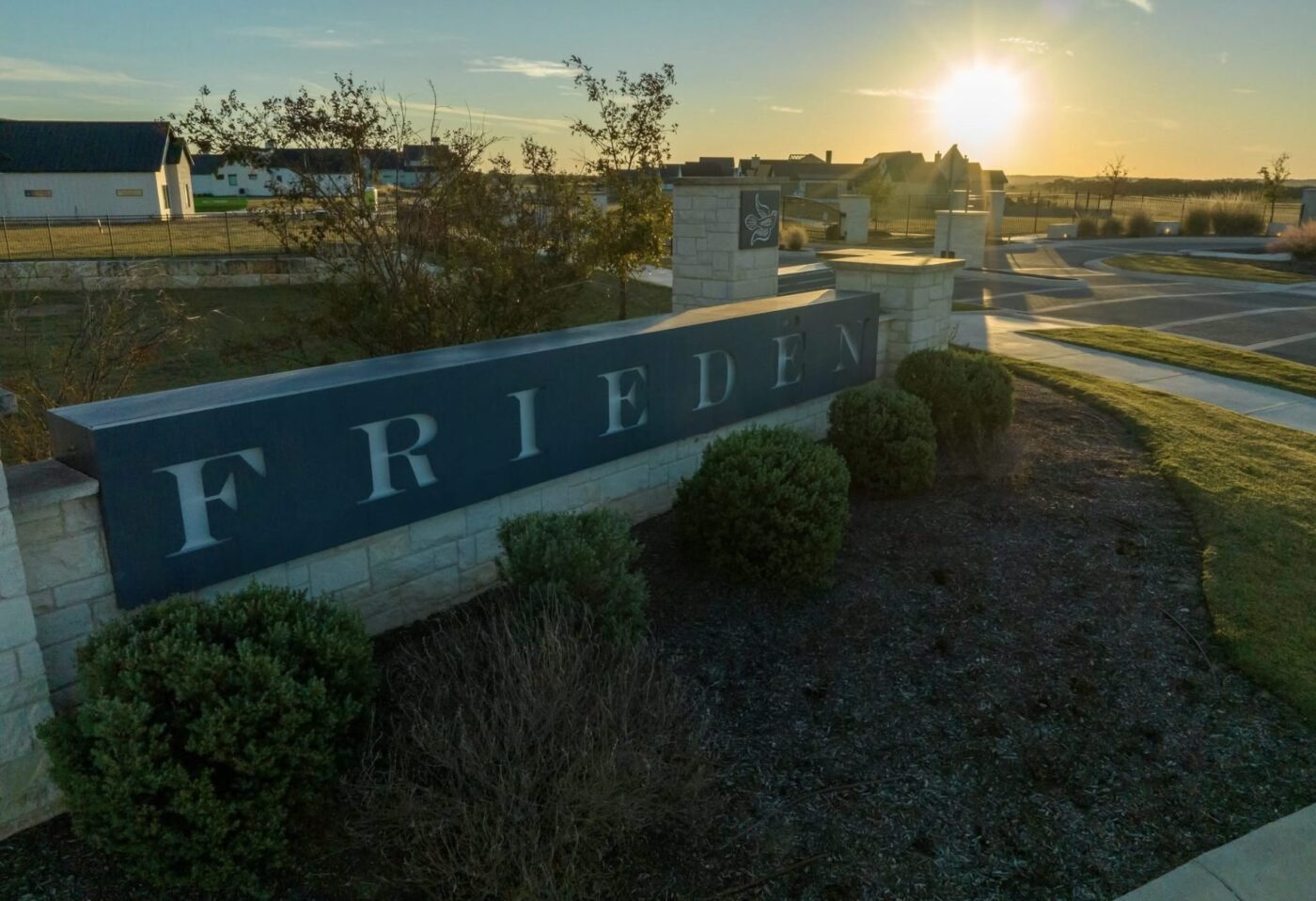 Stone entrance sign reading Friedën at sunset near a gated roadway
