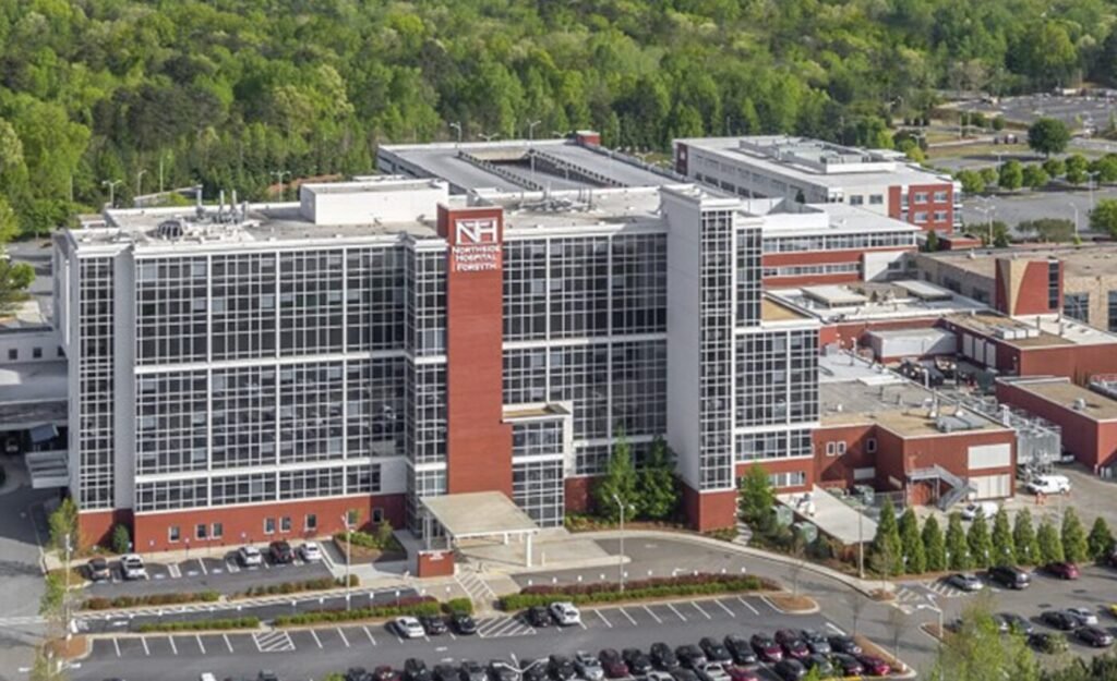 Aerial view of a large hospital building with a glass front, brick accents and surrounding parking lots