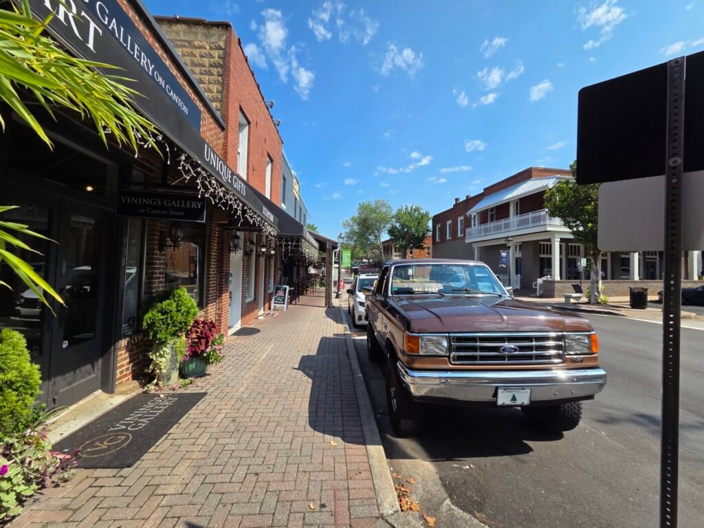 Brick storefronts and parked pickup trucks line a sunny downtown street.