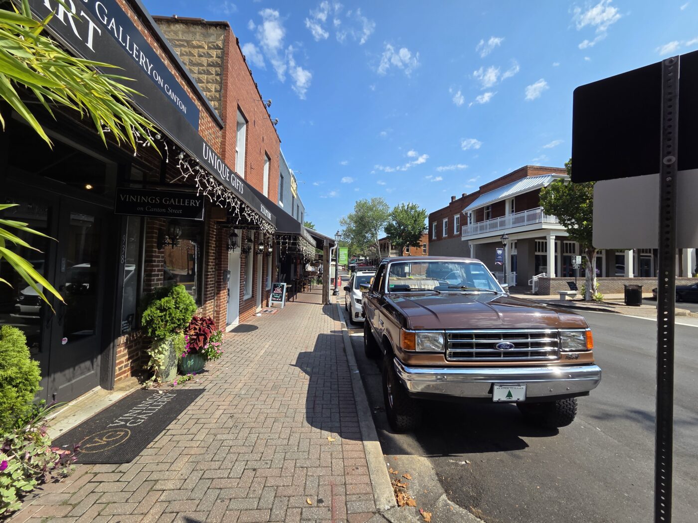 Parked pickup truck along a brick-lined downtown street with storefronts and a blue sky