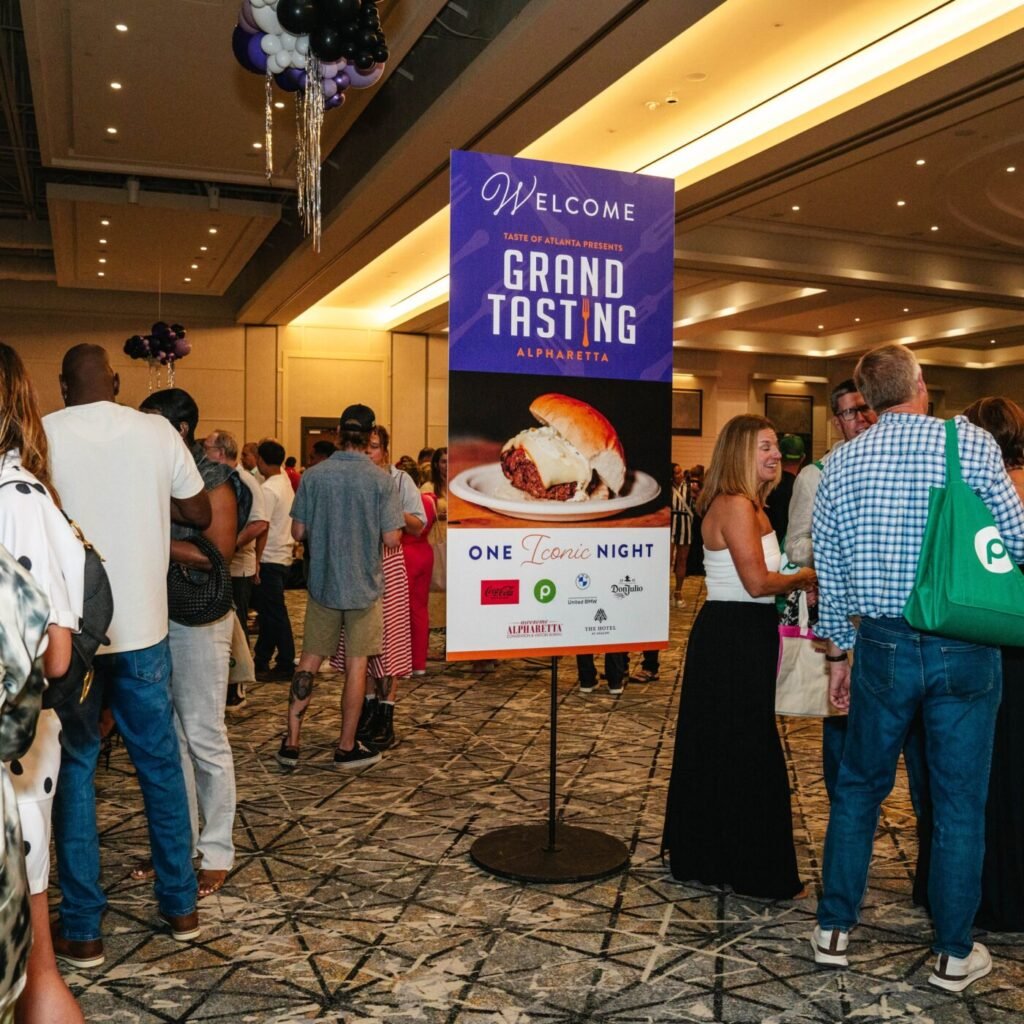 Guests gather in a hotel ballroom around a purple Grand Tasting Alpharetta welcome sign.