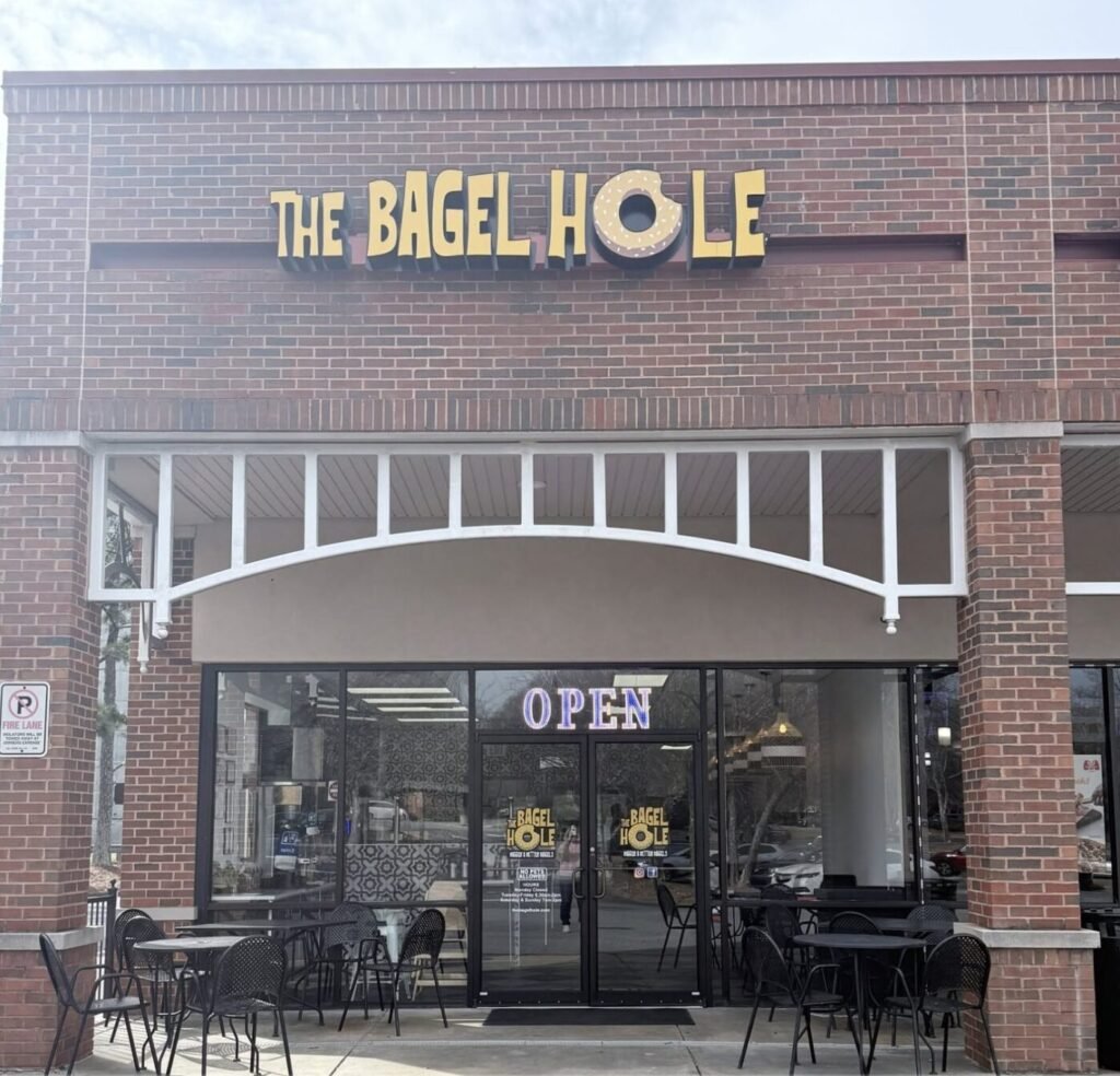 Brick storefront with The Bagel Hole sign above the entrance and an OPEN neon sign in the window