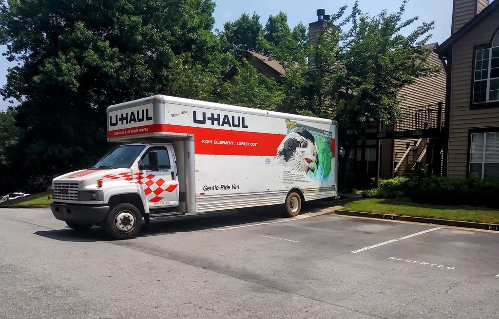 U-Haul moving truck parked in a residential apartment complex lot beside trees and brick buildings.
