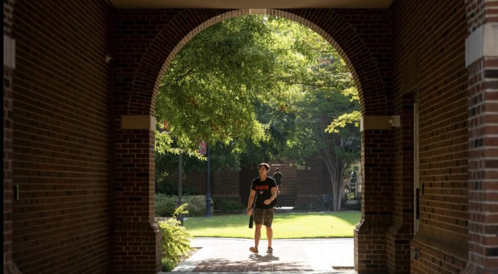 A student walks through a brick archway on a university campus.