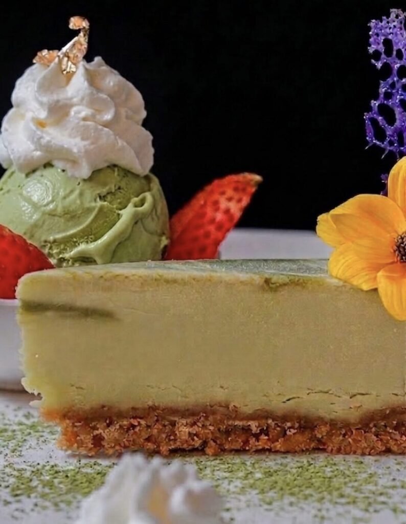 A slice of dessert with green ice cream, whipped cream, strawberries and a flower garnish.