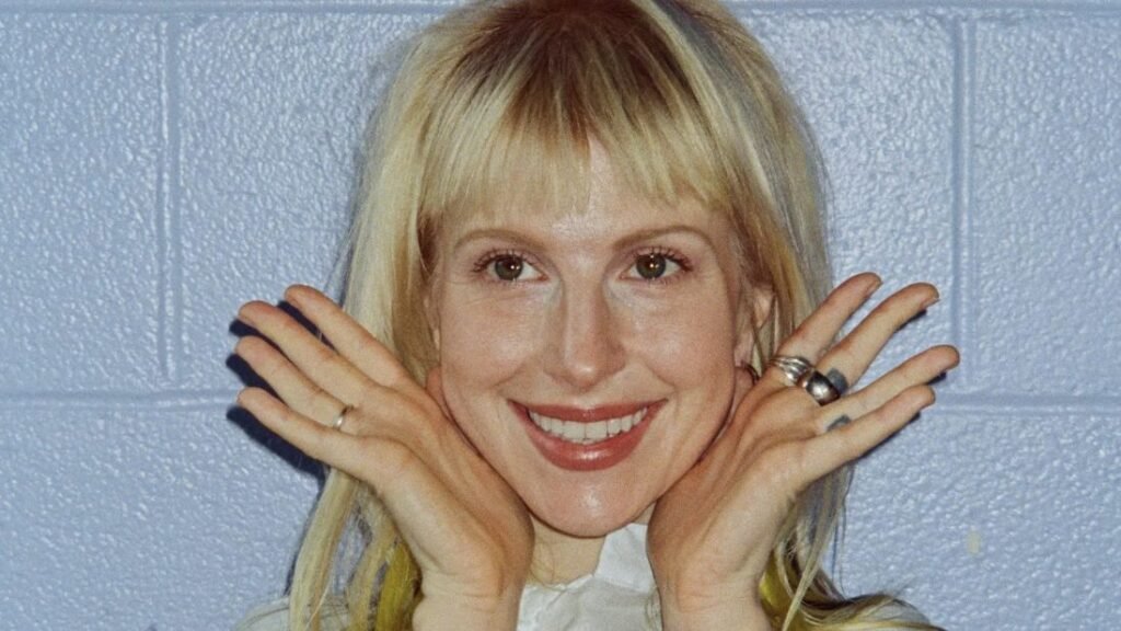 Portrait of a smiling blonde woman with her hands raised near her face.