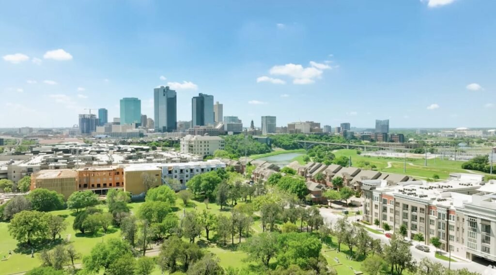 A wide view of a city skyline beyond trees, parkland and low-rise neighborhoods.