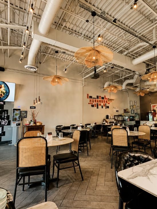 Dining room with round tables, woven chairs and hanging lights inside a restaurant