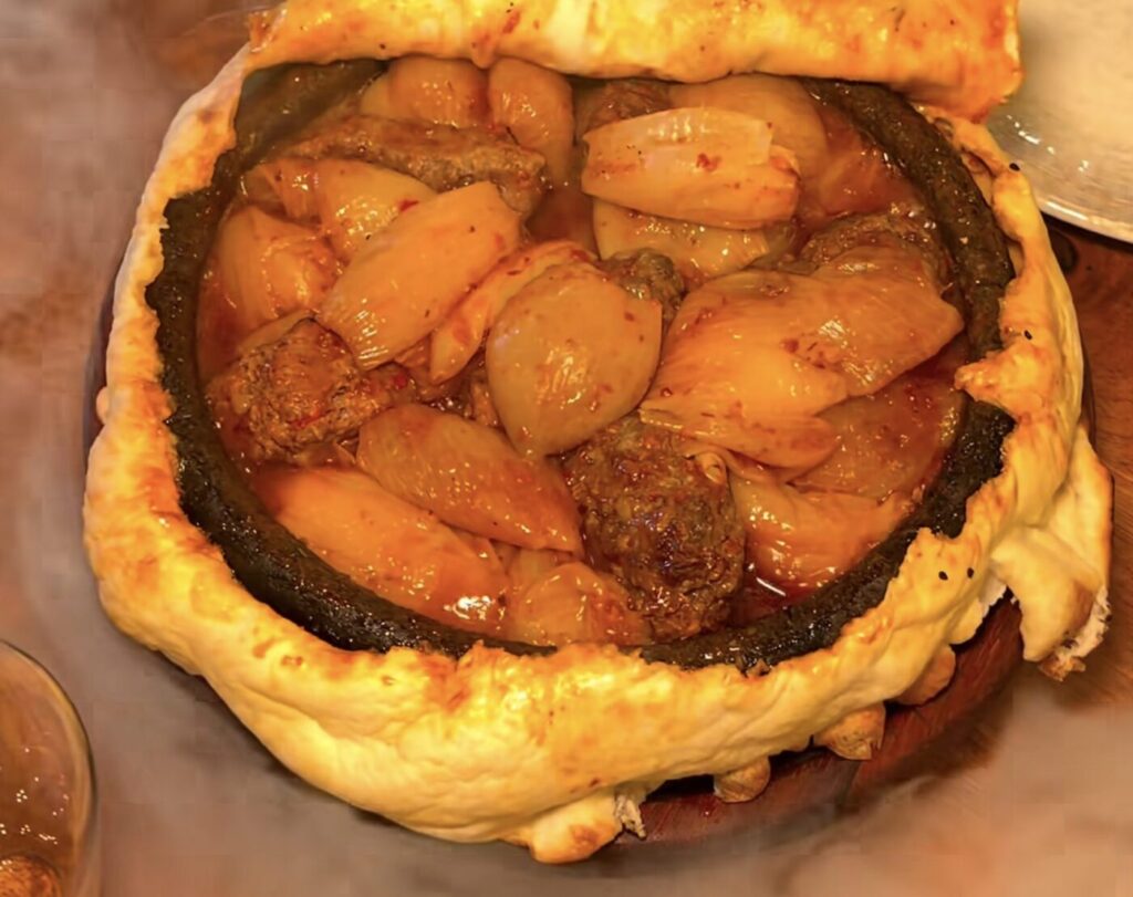 A baked Turkish dish with onions and meat sits inside a ring of bread crust.