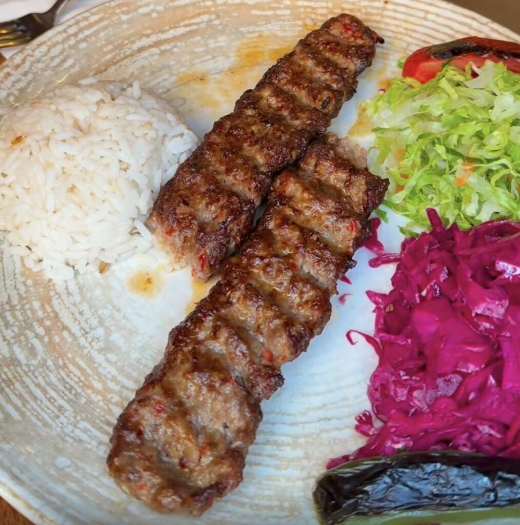 Grilled meat skewers are served with rice and shredded vegetables on a plate.
