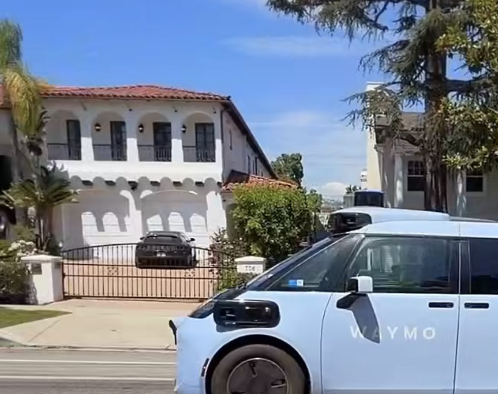 A Waymo vehicle driving past homes on a sunny street.