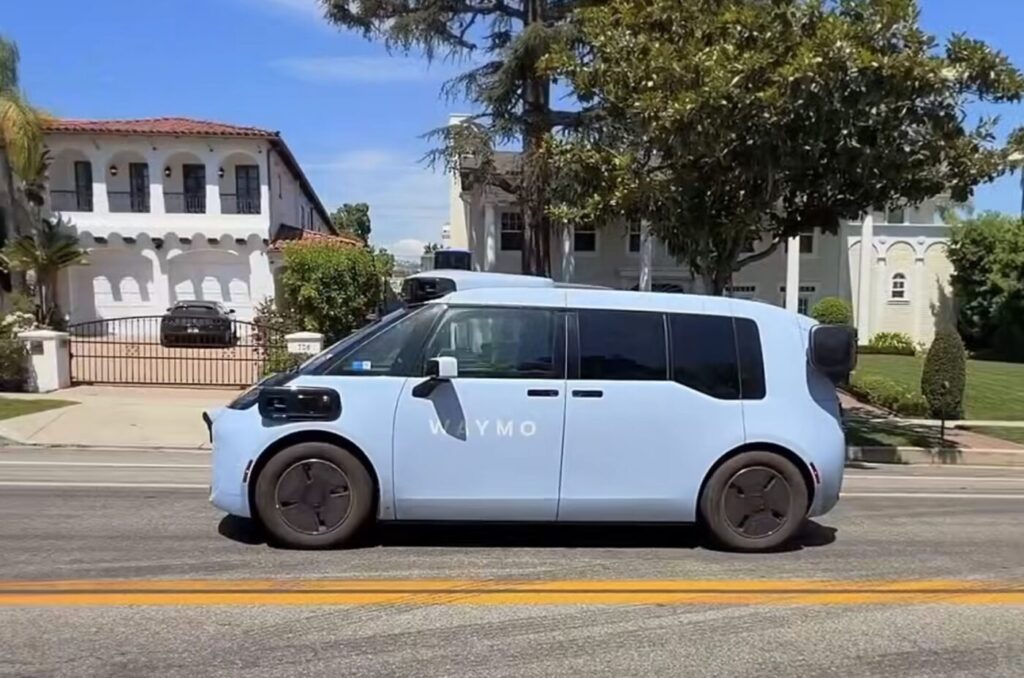 Side view of a light blue Waymo minivan driving on a residential street.