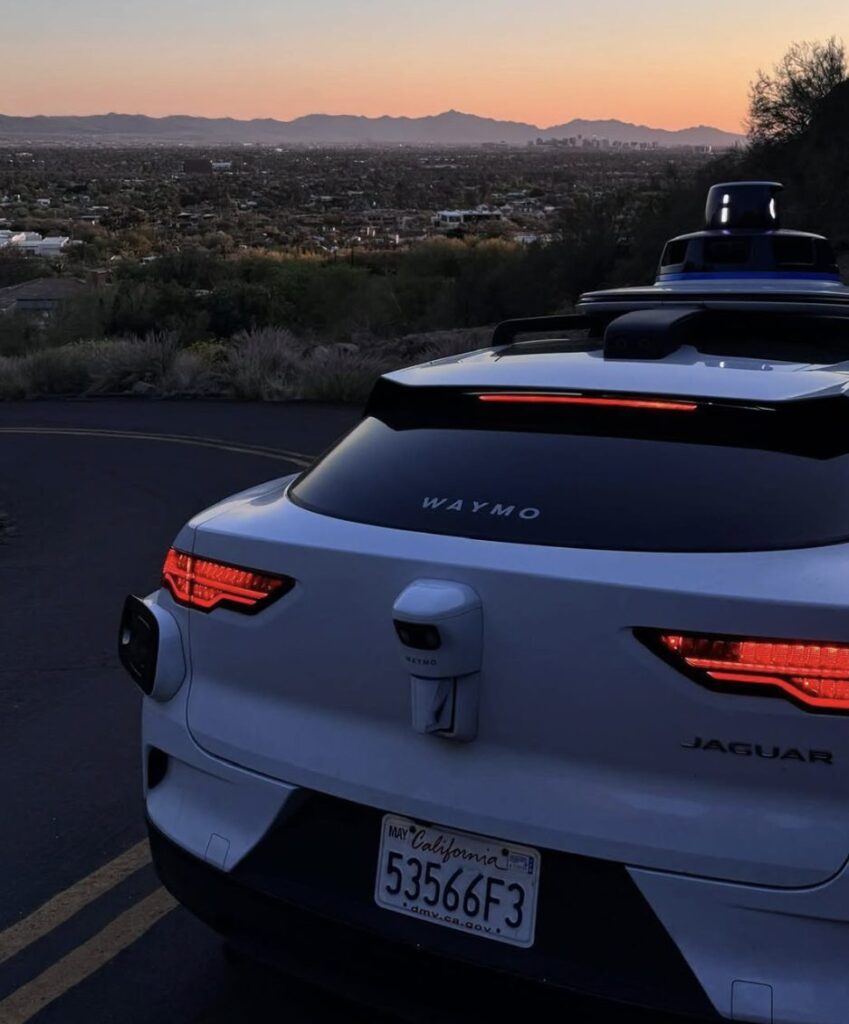 Rear view of a white Waymo Jaguar parked at a scenic overlook with the Golden Gate Bridge in the background.
