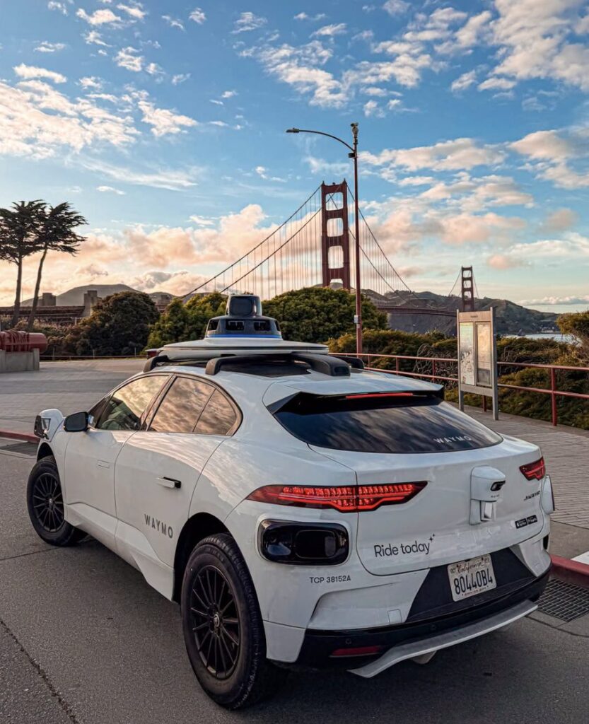 Waymo vehicle parked near the Golden Gate Bridge at sunset.