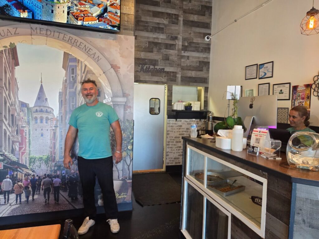 Man standing inside a restaurant beside the counter and a decorative wall mural