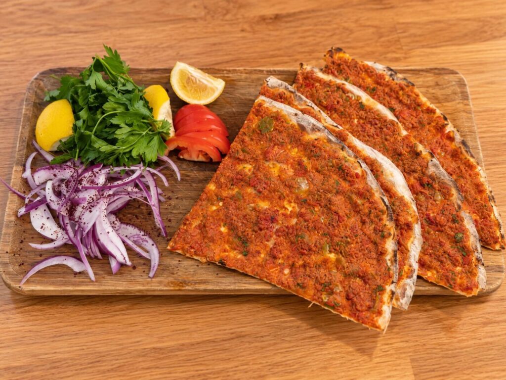 Flatbread pizza slices topped with minced meat, served with herbs, onion, lemon and tomato on a wooden board