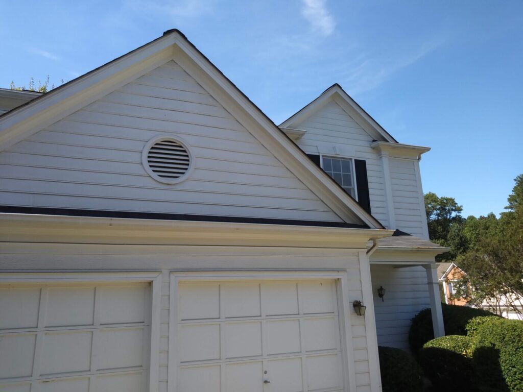 White suburban house with two garage doors, a front gable and visible gutters under a clear blue sky.