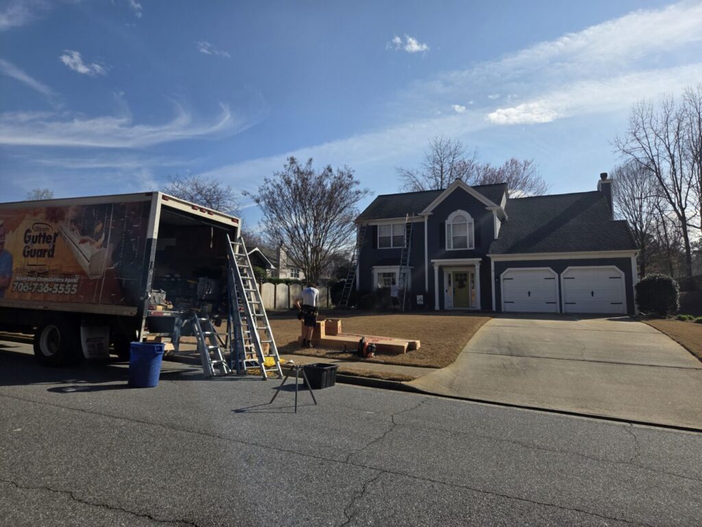 Gutter-cleaning truck, ladders and equipment set up in front of a two-story house.