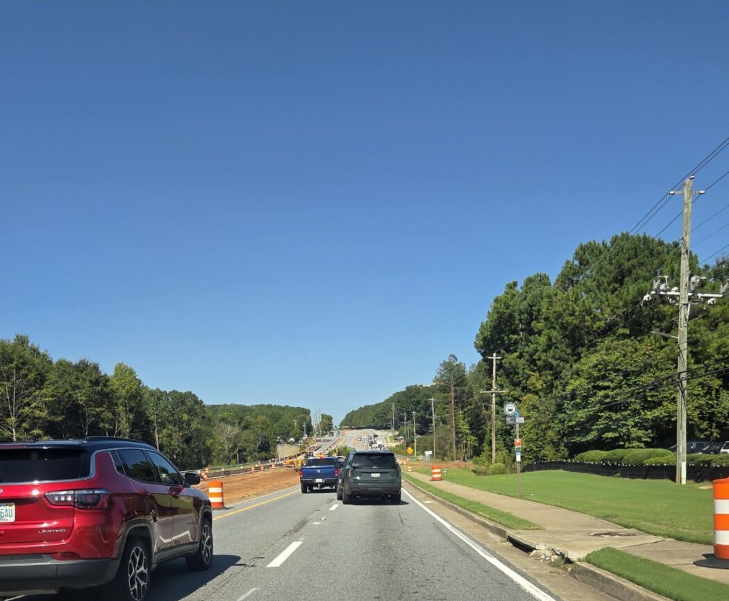 Traffic moves through a work zone on a multilane road lined with orange construction barrels.