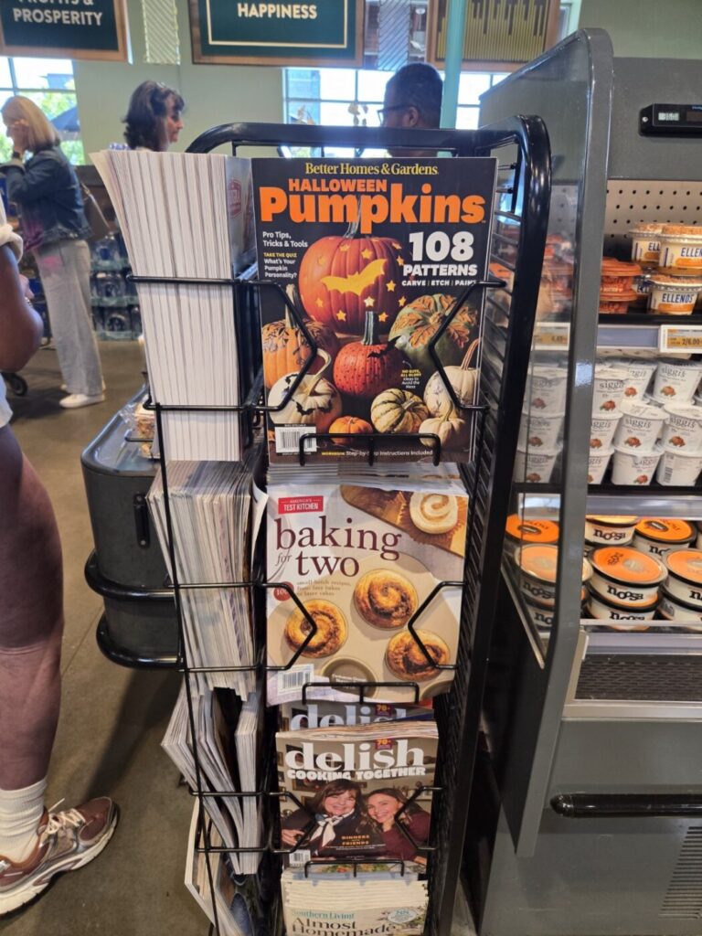 A store magazine rack with Halloween pumpkin magazines and baking magazines beside grocery displays.