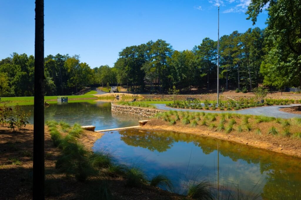A pond with grassy banks, stone edging and a paved path curving along the water.