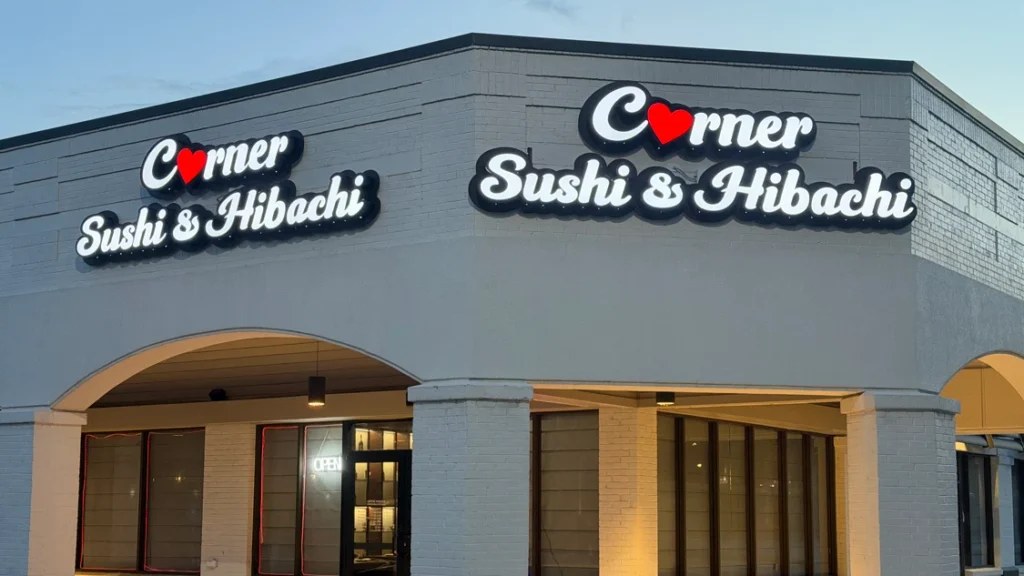 Exterior of Corner Sushi & Hibachi in a strip center at dusk, with illuminated storefront signs above arched entrances