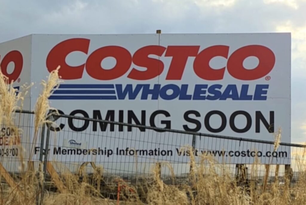 A Costco Wholesale sign reads 'Coming Soon' behind a fence and tall grass.