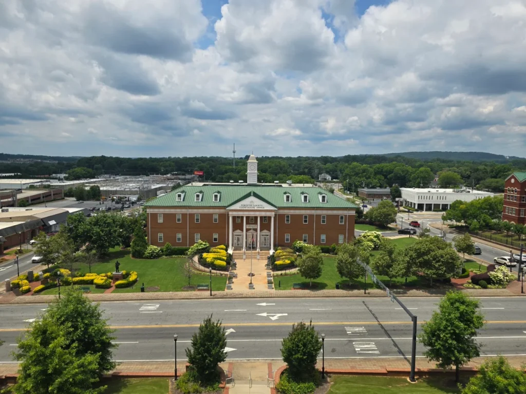Brick courthouse building with a green roof and clock tower, landscaped lawn, and cloudy sky
