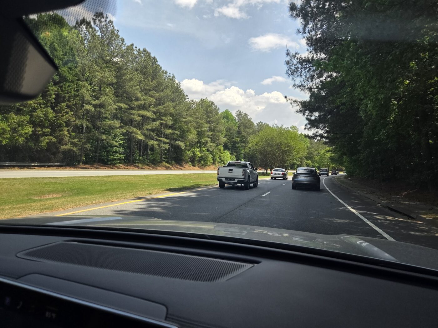 View from inside a car on a multi-lane road with several vehicles ahead and trees lining both sides.