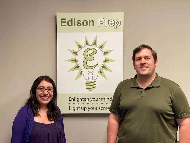 Two people standing beside an Edison Prep sign on a beige wall.